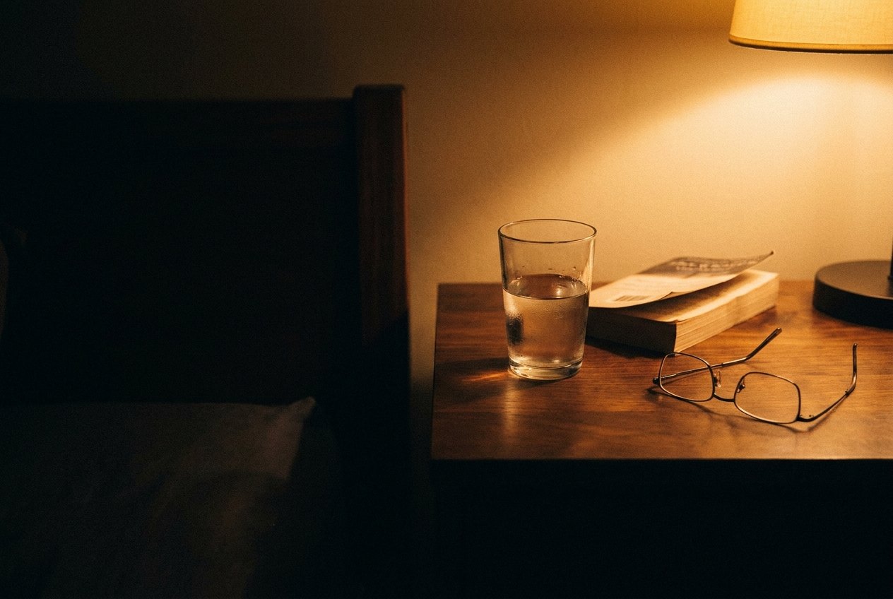 An adult reading the Supplement Facts panel on a closed Soft Friday Daily Foundation Multivitamin bottle beside a glass of water